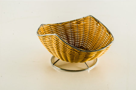 A basket made of woven material sits on a white surface. The basket is small and has a curved shapeの写真素材