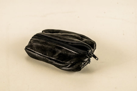 A black purse with a zipper on the side. It is sitting on a white surface. The purse is emptyの写真素材