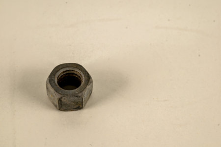 A small silver nut sits on a white surface. The nut is slightly worn and has a few scratches on it. Concept of wear and tear, as well as the passage of timeの写真素材