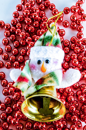 A snowman with a bell on his hat is sitting on a red and gold string of beads. The snowman is wearing a green and red scarf, and his eyes are closedの写真素材