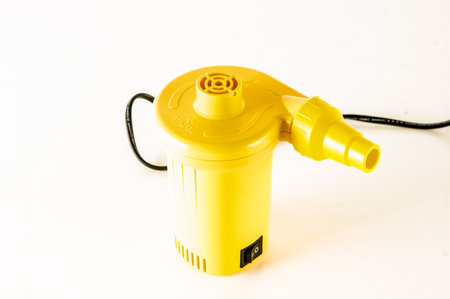A yellow and black air compressor sits on a white surface. The air compressor is plugged into a wall outletの写真素材