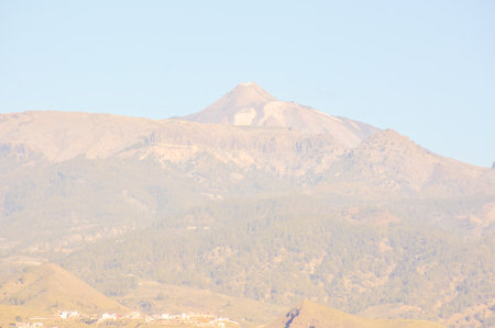 A mountain with a cloudy sky in the background. The mountain is covered in trees and has a rocky surfaceの写真素材