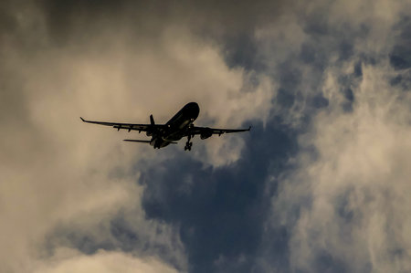 A jet plane is flying through a cloudy sky. The sky is dark and the clouds are thick, creating a moody atmosphereの写真素材