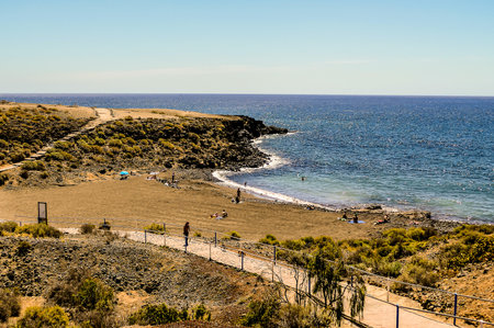 A beach with a few people walking along a path. The beach is sandy and the ocean is blueの写真素材