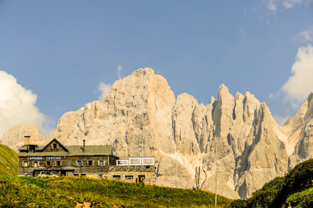A mountain range is in the background of a small house. The house is surrounded by a lush green fieldの写真素材
