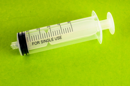 A syringe is sitting on a green surface. The syringe is labeled for single use. The syringe is made of plastic and has a black capの写真素材