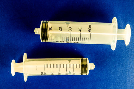 Two syringes are on a blue background. One is labeled with a number of 20. The other is labeled with a number of 30の写真素材