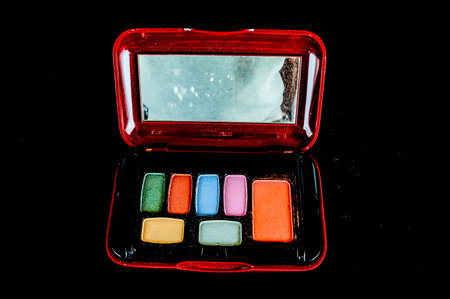 A small red makeup case with a mirror inside. The case is filled with a variety of colorful eyeshadowsの写真素材