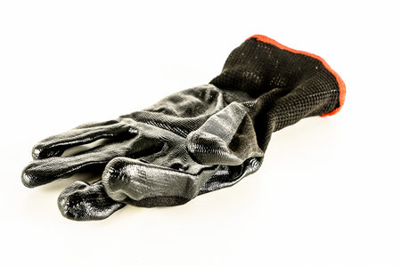 A black glove with a red band is laying on a white surface. The glove is worn and torn, and the red band is frayed. Concept of weariness and neglectの写真素材