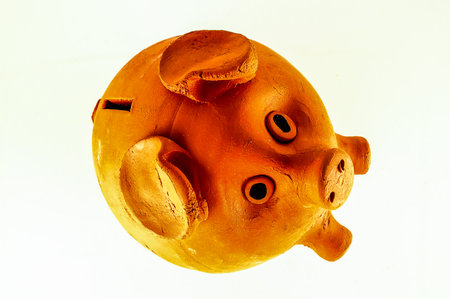 A piggy bank is sitting on a white background. The piggy bank is made of clay and has a brown colorの写真素材
