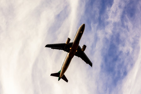 A large airplane is flying through a cloudy sky. The sky is mostly blue with some clouds scattered throughout. The airplane is the main focus of the image, and it is soaring through the air with easeの写真素材