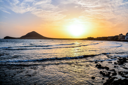 The sun is setting over the ocean, casting a warm glow over the water. The sky is filled with clouds, creating a serene and peaceful atmosphere. The waves gently lap against the shoreの写真素材