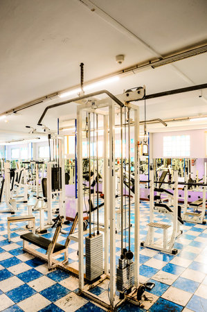 A gym with a lot of equipment, including a weight machine. The room is mostly empty, with only a few people visible in the background. The atmosphere is quiet and focusedの写真素材