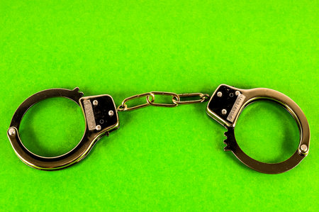 Two handcuffs are chained together on a green surface. The handcuffs are made of metal and are black in color. Concept of authority and controlの写真素材