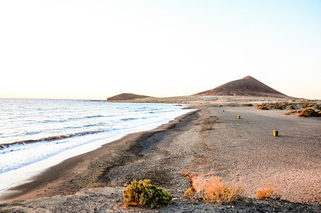 A beach with a mountain in the background. The beach is empty and the sky is blueの写真素材