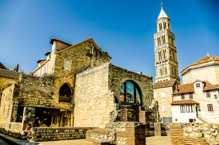A stone building with a tall tower in the background. The building has a large window and a small window. The sky is blue and clearの写真素材