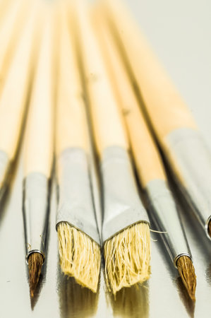 A row of paintbrushes with the middle one being the most prominent. The brushes are all wooden and have a tan colorの写真素材