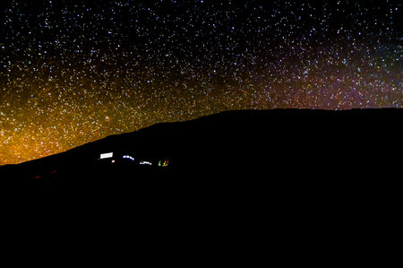 A dark sky with a few stars and a hill in the background. The hill is covered in trees and the sky...