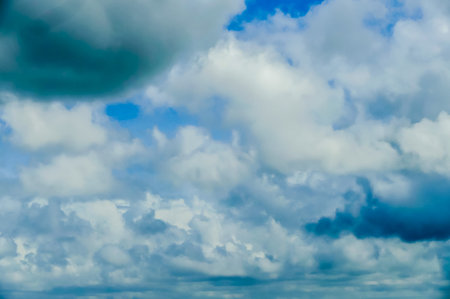 The sky is filled with clouds, and the sun is shining through them. The clouds are white and fluffy, and they cover the entire skyの写真素材