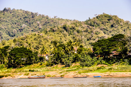 A beautiful mountain range with a lush green forest and a river running through it. The scene is peaceful and serene, with a few boats floating on the waterの写真素材