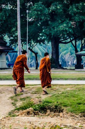 Two monks walking in a park. One of them is wearing a brown robe. The other monk is wearing a brown robe and has a white sandal onの写真素材