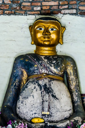 A statue of a man with a gold belly is sitting on a wall. The statue is old and has a worn appearanceの写真素材