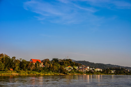 A beautiful blue sky with a few clouds and a small town in the background. The town is surrounded by a river and a forestの写真素材