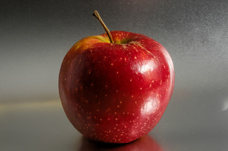A red apple sits on a table. The apple is shiny and has a stem. The apple is ripe and ready to eatの写真素材