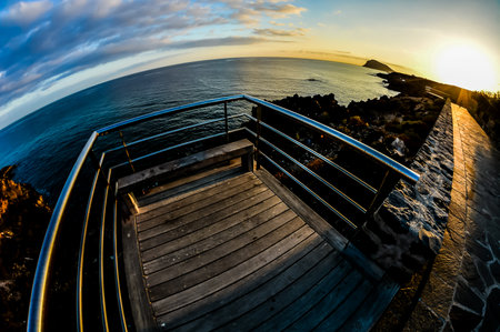 A view of the ocean from a wooden platform. The sun is setting in the backgroundの写真素材