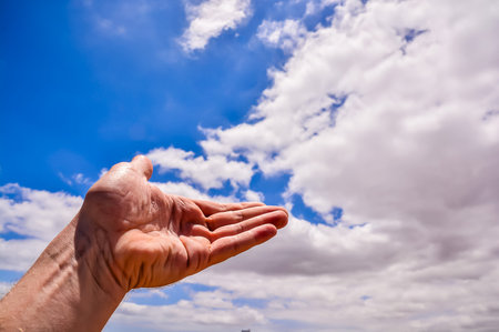 A hand is raised in the air, with the sky behind it. The sky is blue and cloudy, and the hand is wetの写真素材
