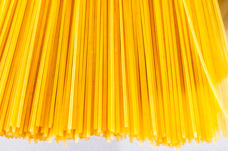 A bunch of yellow noodles are piled up on a white background. The noodles are long and thin, and they are all the same color. The image has a simple and straightforward lookの写真素材