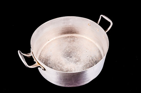 A silver pan is sitting on a black background. The pan is empty and has a worn appearanceの写真素材