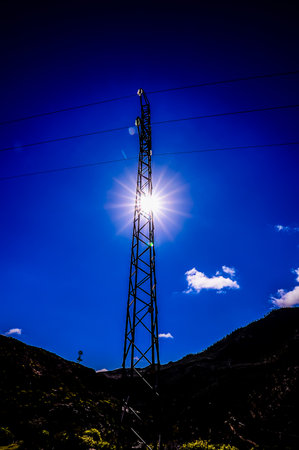 A tall power pole is silhouetted against a blue sky. The sun is shining brightly, casting a warm glow on the pole. The scene is peaceful and serene, with the power pole standing tallの写真素材