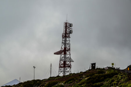 A tall tower with a red and white top sits on a hill. The sky is cloudy and the weather is overcastの写真素材