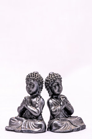 Two silver statues of Buddha sitting on their knees. The statues are identical and are facing each otherの写真素材