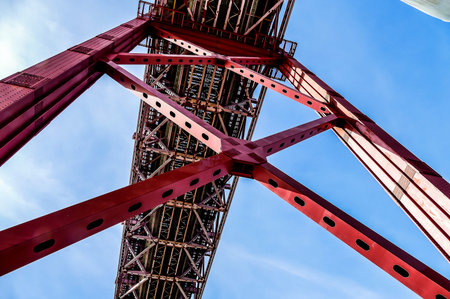 A red bridge with a blue sky in the background. The bridge is very tall and has a lot of metal