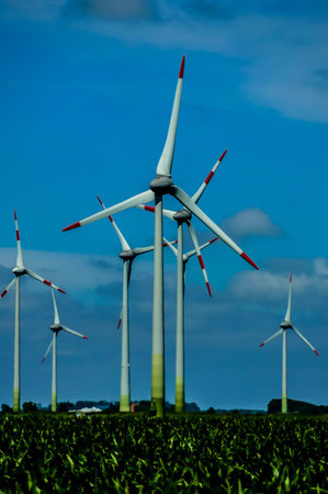 A row of wind turbines are standing in a field. The windmills are tall and have a red and white...