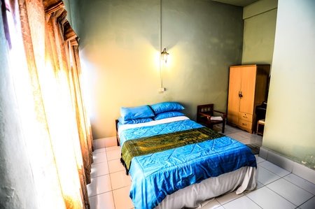 A bedroom with a blue and white bed and a chair. The room is bright and sunny, with a window letting in natural lightの写真素材