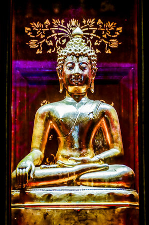 A gold statue of a Buddha sitting in a lotus position. The statue is surrounded by a purple backgroundの写真素材