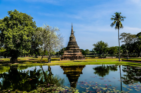 A beautiful pond with a small temple in the background. The pond is surrounded by trees and the temple is a small structure with a tall tower. The scene is peaceful and sereneの写真素材