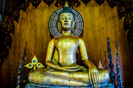 A gold statue of a Buddha sitting on a wooden platform. The statue is surrounded by candles and other objectsの写真素材