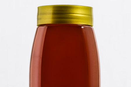 A bottle of honey is shown with a gold lid. The bottle is sitting on a white backgroundの写真素材