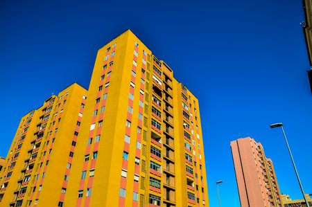 A row of yellow buildings with a blue sky in the background. The buildings are tall and have many windowsの写真素材