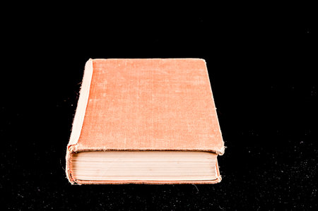 A book with a tan cover is laying on a black background. The book is open to the middle of the pageの写真素材