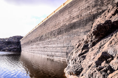 A rocky cliff is next to a body of water. The water is calm and the rocks are jagged. The scene is peaceful and sereneの写真素材