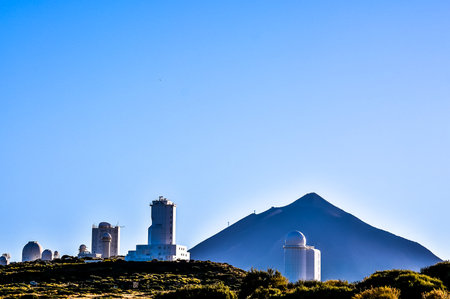 A mountain is in the background of a picture of a group of buildings. The buildings are white and are located on a hillの写真素材