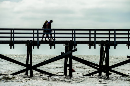 A couple walking on a pier with the water in the background. Scene is peaceful and romanticの写真素材