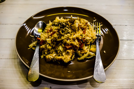 A plate of rice with a fork and spoon on it. The spoon is on the left side of the plate and the fork is on the rightの写真素材