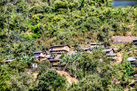 A lush green hillside with a village of small homes. The houses are made of wood and are clustered together. The village is surrounded by trees and the sky is clear. The scene is peaceful and sereneの写真素材