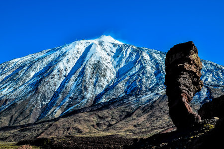 A mountain with snow on it and a large rock in the foregroundの写真素材